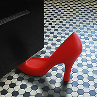 Red Fred Foot in the Door Door Stop wedged in black door on black and white tiled floor